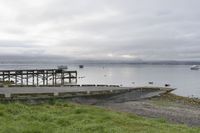 a pier sits empty on a cloudy day, overlooking the water with boats out to sea