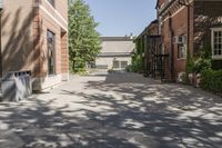 an empty brick courtyard with fire escapes in the background and trees and buildings lining the walkway