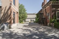 an empty brick courtyard with fire escapes in the background and trees and buildings lining the walkway