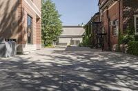 an empty brick courtyard with fire escapes in the background and trees and buildings lining the walkway