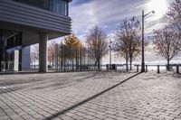 an empty brick pathway in front of a building with benches on the pavement near by