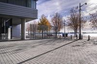 an empty brick pathway in front of a building with benches on the pavement near by