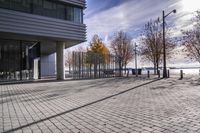 an empty brick pathway in front of a building with benches on the pavement near by