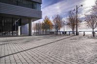 an empty brick pathway in front of a building with benches on the pavement near by