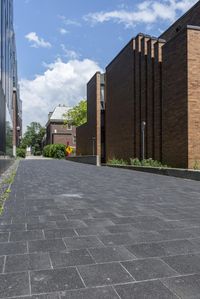 an empty brick road in front of tall brown buildings on a sunny day with a red and yellow umbrella near the side of it