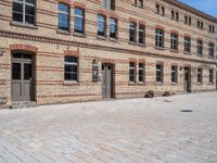 an empty brick sidewalk outside a large building that is near a clock tower in front