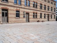 an empty brick sidewalk outside a large building that is near a clock tower in front