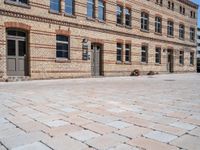 an empty brick sidewalk outside a large building that is near a clock tower in front