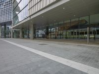 a empty brick sidewalk in front of a building with an entrance and glass walls and a sign attached