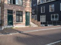 an empty brick street lined with buildings and a person skateboarding with their board in front of them