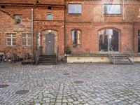 an empty brick street with stairs and steps to the side of a building filled with windows