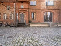 an empty brick street with stairs and steps to the side of a building filled with windows