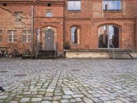 an empty brick street with stairs and steps to the side of a building filled with windows