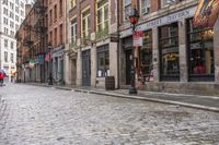 an empty brick street with many businesses on it and two people on the sidewalk walking down the road