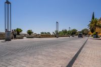 empty bricked sidewalk with palm trees and benches in it under a blue sky at an outdoor park