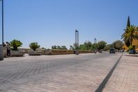 empty bricked sidewalk with palm trees and benches in it under a blue sky at an outdoor park