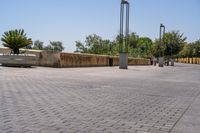 empty bricked sidewalk with palm trees and benches in it under a blue sky at an outdoor park