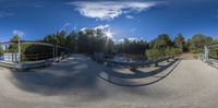 a 360 - camera image shows an empty bridge with the sun in the background and blue sky over trees on both sides