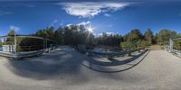 a 360 - camera image shows an empty bridge with the sun in the background and blue sky over trees on both sides