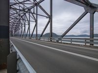 an empty bridge over water on a cloudy day with blue sky and some mountains in the background