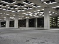 an empty building with two floors in front of a parking lot with columns and lights on