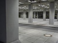 a tiled walkway is in a very large, empty building with concrete flooring and exposed ceiling