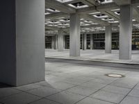 a tiled walkway is in a very large, empty building with concrete flooring and exposed ceiling