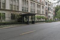 an empty bus stop next to a city street with tall buildings on both sides of it