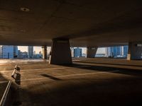 an empty car park under a highway with tall buildings in the background and a person standing on one side