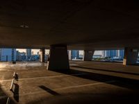 an empty car park under a highway with tall buildings in the background and a person standing on one side