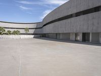 a view of an empty cement building from a parking lot with lots of parked cars