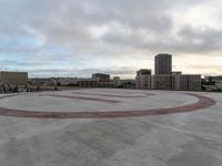 an empty circular parking lot with some buildings and clouds in the background in front of it