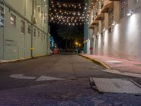 empty city alley with a row of buildings lit up with string lights at night time