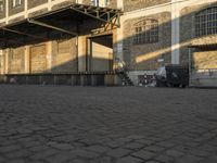 the empty city block of an old industrial area with a bench, trashcan and dog looking out