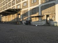 the empty city block of an old industrial area with a bench, trashcan and dog looking out