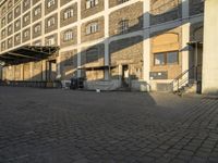 the empty city block of an old industrial area with a bench, trashcan and dog looking out