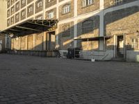 the empty city block of an old industrial area with a bench, trashcan and dog looking out