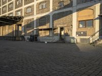 the empty city block of an old industrial area with a bench, trashcan and dog looking out