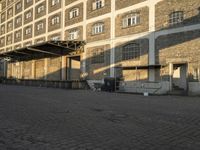 the empty city block of an old industrial area with a bench, trashcan and dog looking out