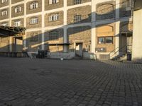 the empty city block of an old industrial area with a bench, trashcan and dog looking out