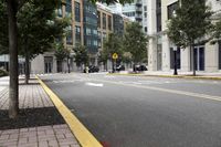 empty city street next to a large building with a yellow sign on one corner and street marked with white lines