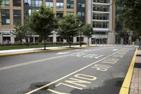 empty city street next to a large building with a yellow sign on one corner and street marked with white lines