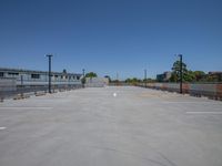 an empty parking lot with a fence near by buildings and lights on a clear blue sky day