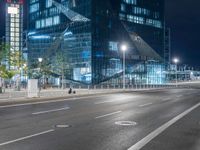 an empty city road at night with a big building behind it and a bus on the side