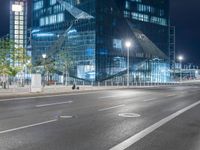 an empty city road at night with a big building behind it and a bus on the side