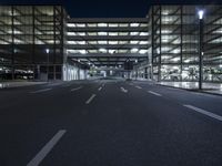 a empty empty city road at night with street lights shining behind it and an illuminated garage on the left side of the road