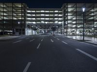 a empty empty city road at night with street lights shining behind it and an illuminated garage on the left side of the road