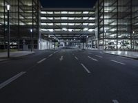 a empty empty city road at night with street lights shining behind it and an illuminated garage on the left side of the road