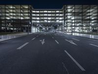 a empty empty city road at night with street lights shining behind it and an illuminated garage on the left side of the road