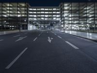 a empty empty city road at night with street lights shining behind it and an illuminated garage on the left side of the road